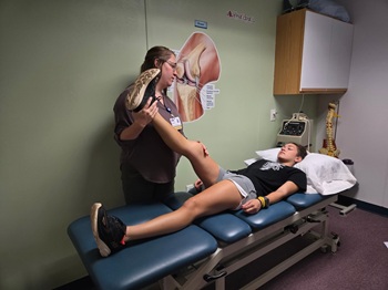 A Nurse is helping a male patient stretch his leg in Rehab