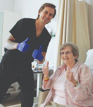 Female patient sitting icn a chair with a male nurse standing beside her.